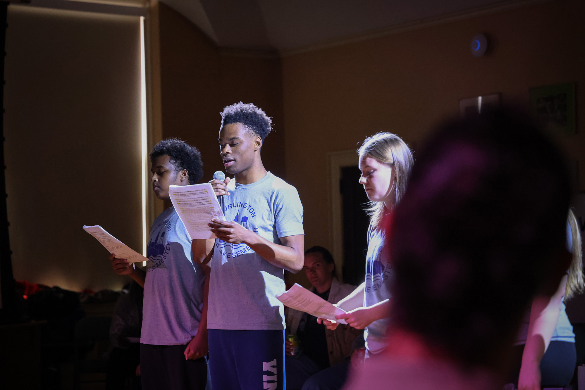 Three young people stand under a spotlight in a community theater space