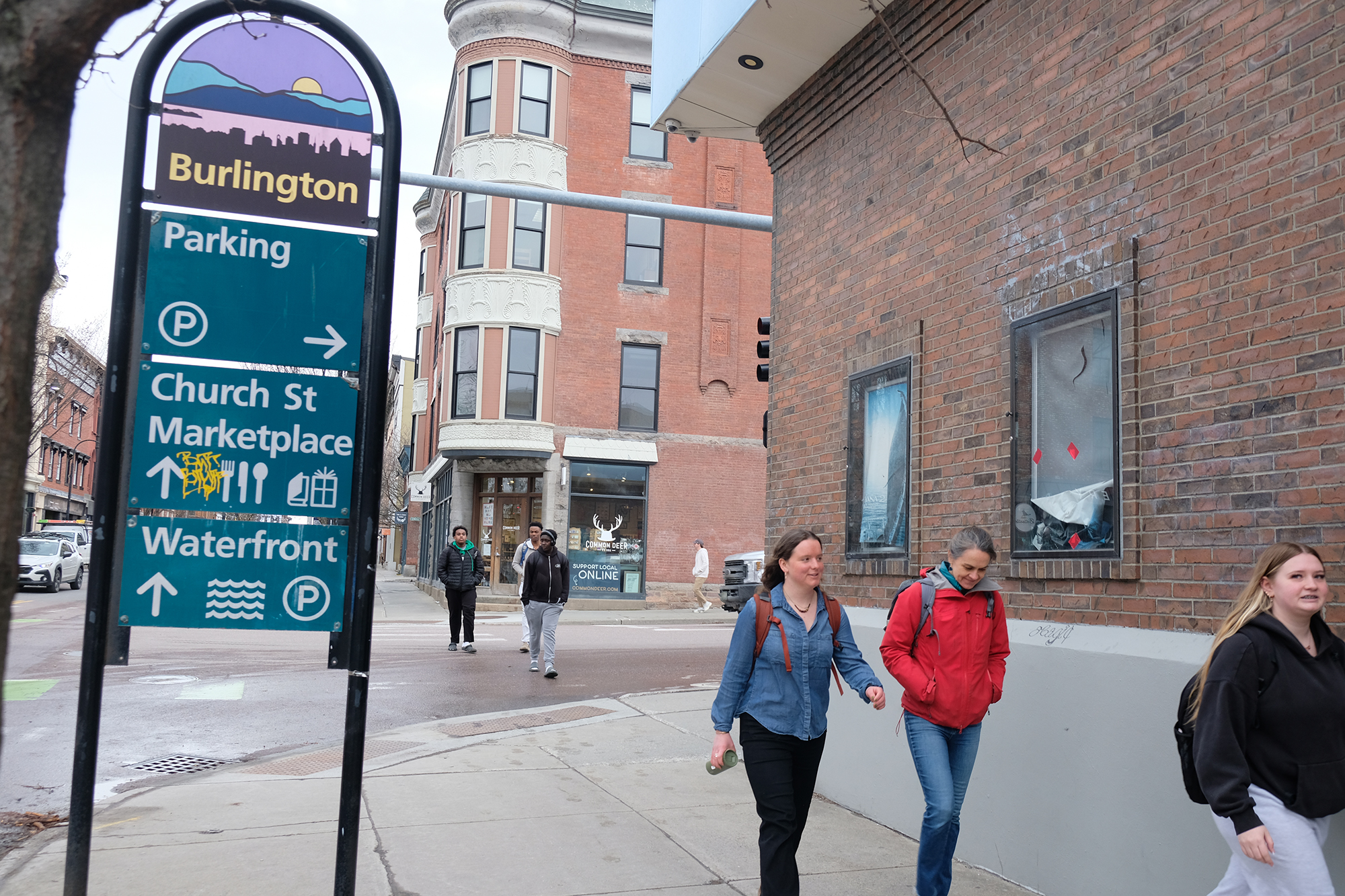 Six people walk on a city sidewalk beneath a Burlington sign