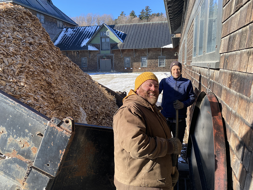 two men beside a truckbed of chipped wood as chips are unloaded