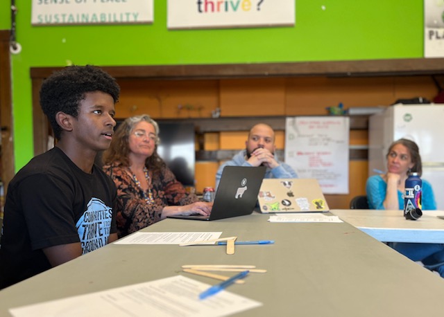 A young person and three adults sit around a classroom table in discussion
