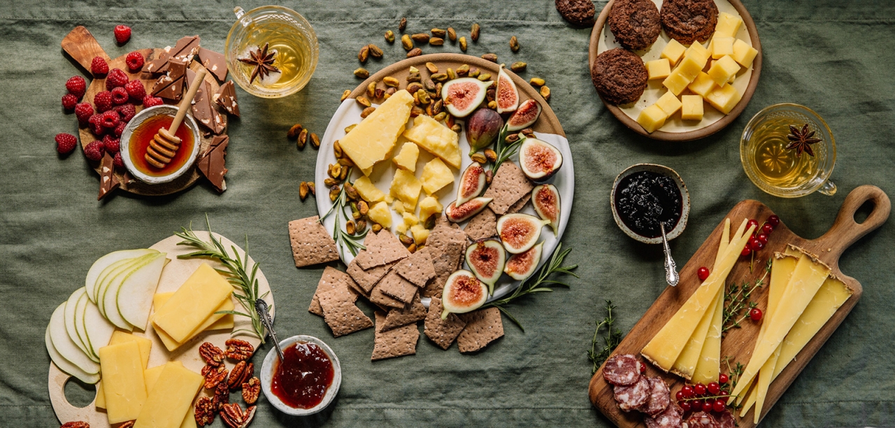 overhead view of plated cheeses, nuts, meats, crackers on green tablecloth