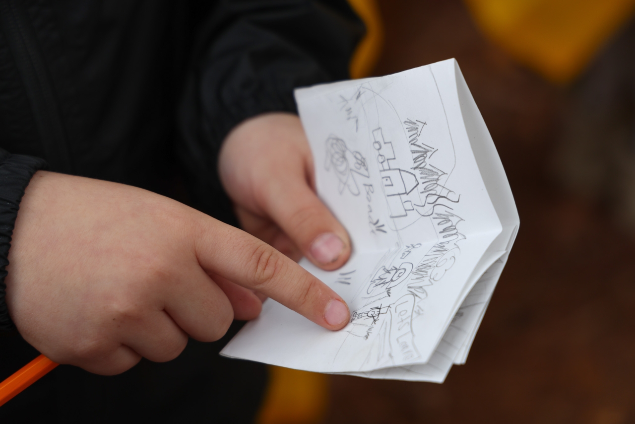 A closeup of a young child's hands holding a small journal depicting a pencil illustration of climate change effects on local landscape.