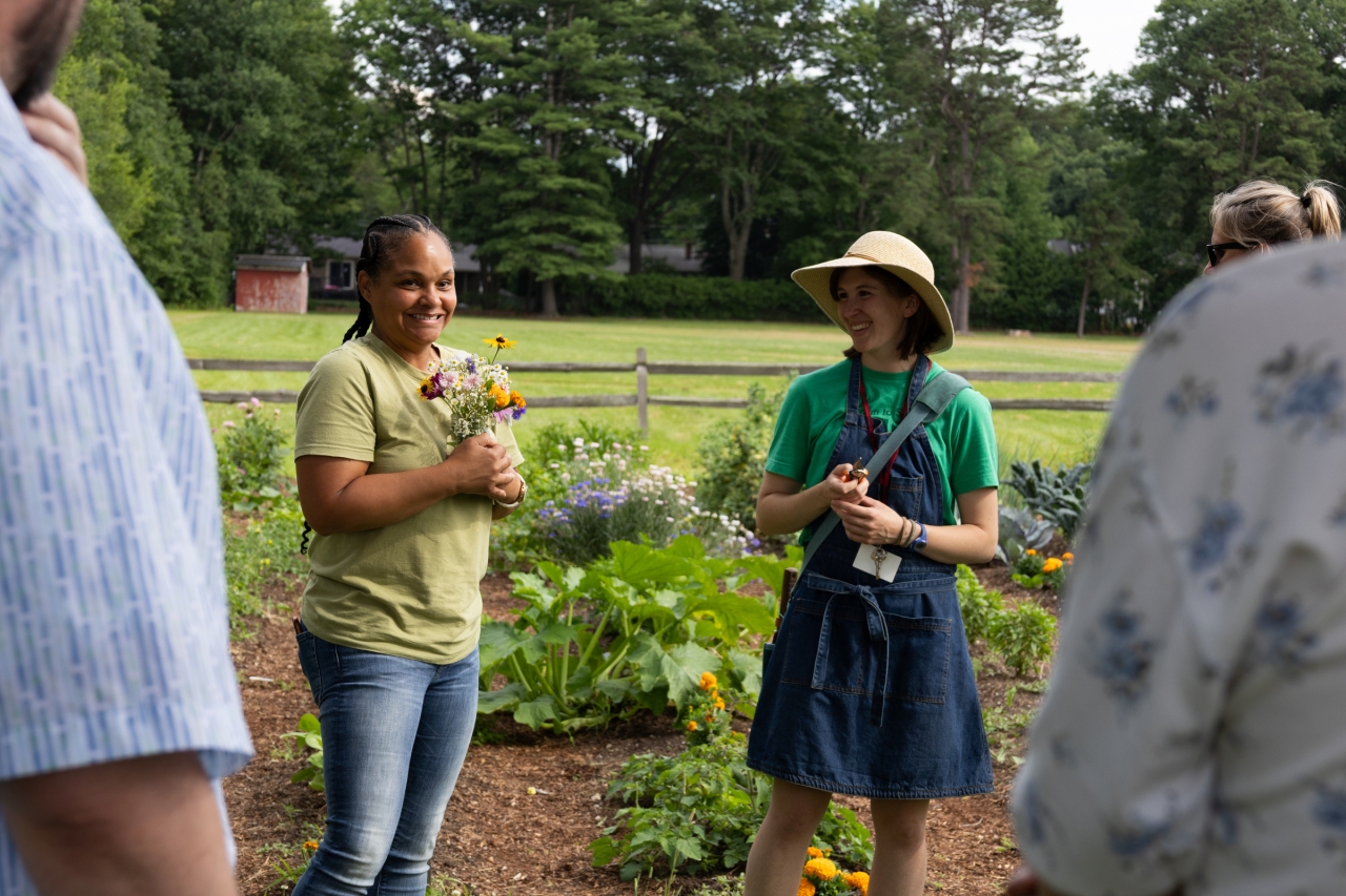 A small group of people smile in a school garden in summertime holding small flower bouquets
