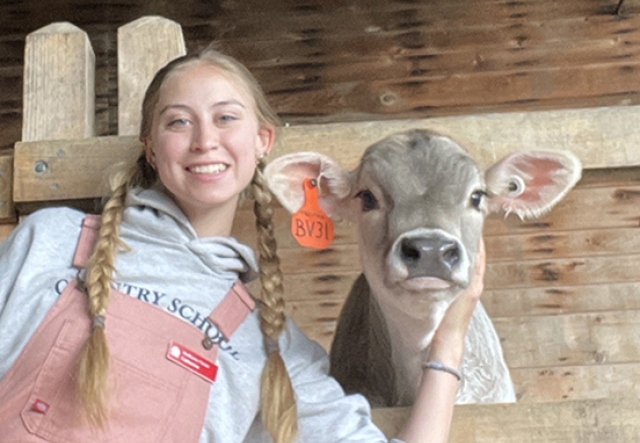 woman with long braids smiling with arm around a calf