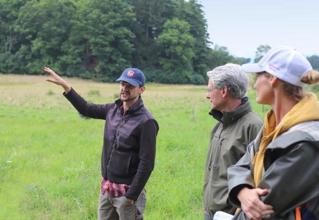 Man in a field gesturing and talking to several other people.