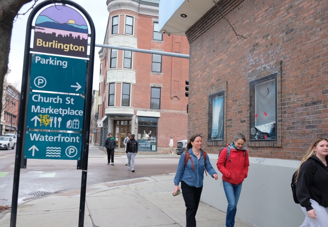 Six people walk along a city sidewalk under a Burlington street sign