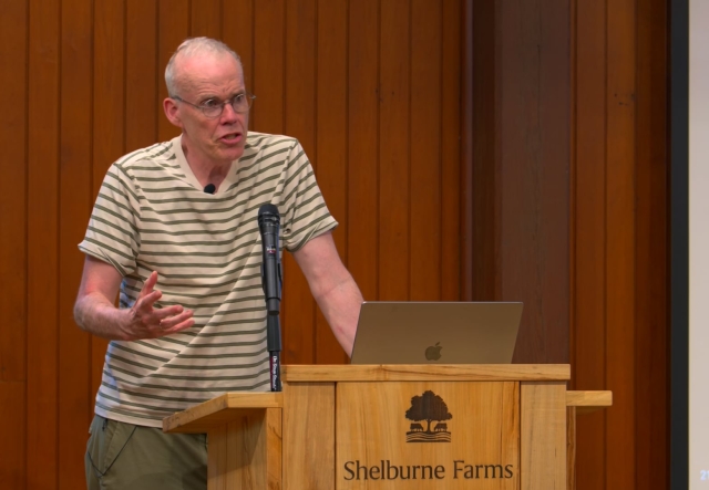 Balding man in glasses and short sleeve button up shirt speaks at a podium