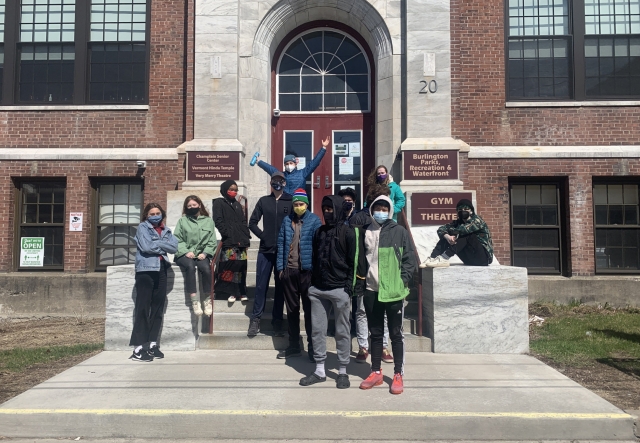 A group of high school aged students poses in front of a large brick building