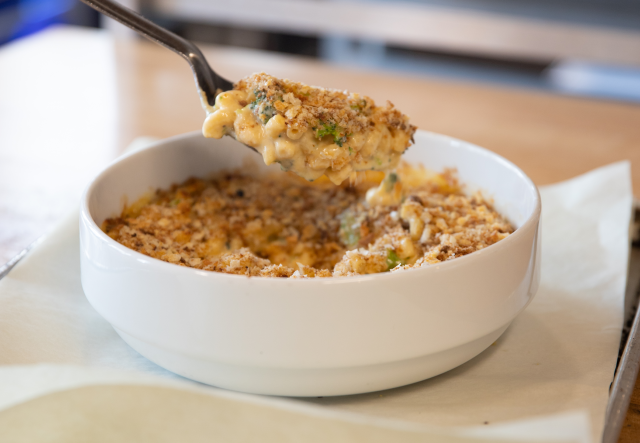 a bowl of macaroni and cheese and broccoli, a spoon pulls out a big scoop from the center